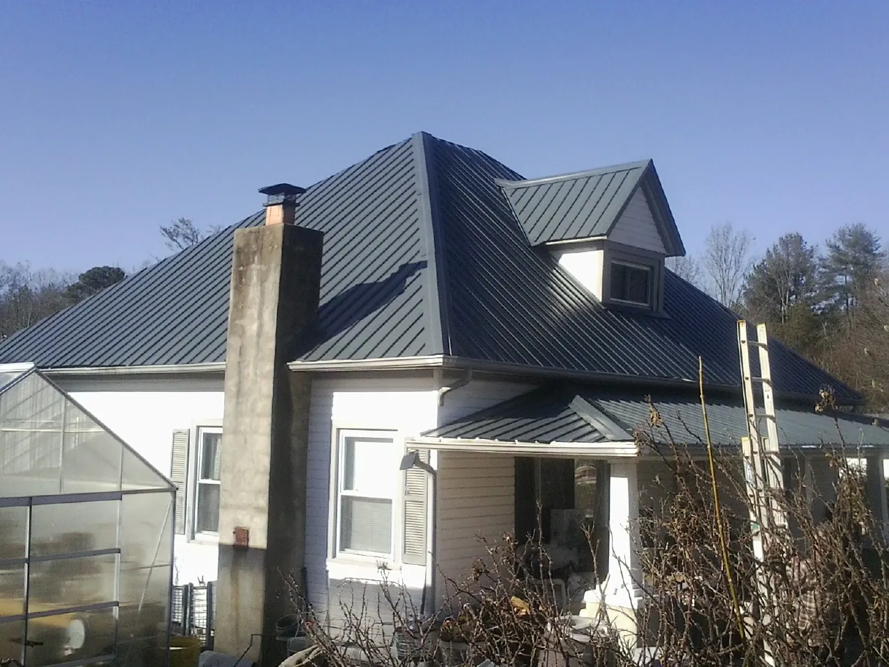 Dark blue standing seam metal roof on a white farmhouse with dormer — Slate & Tile Roof Repair by Roofing Brothers in Dennison
