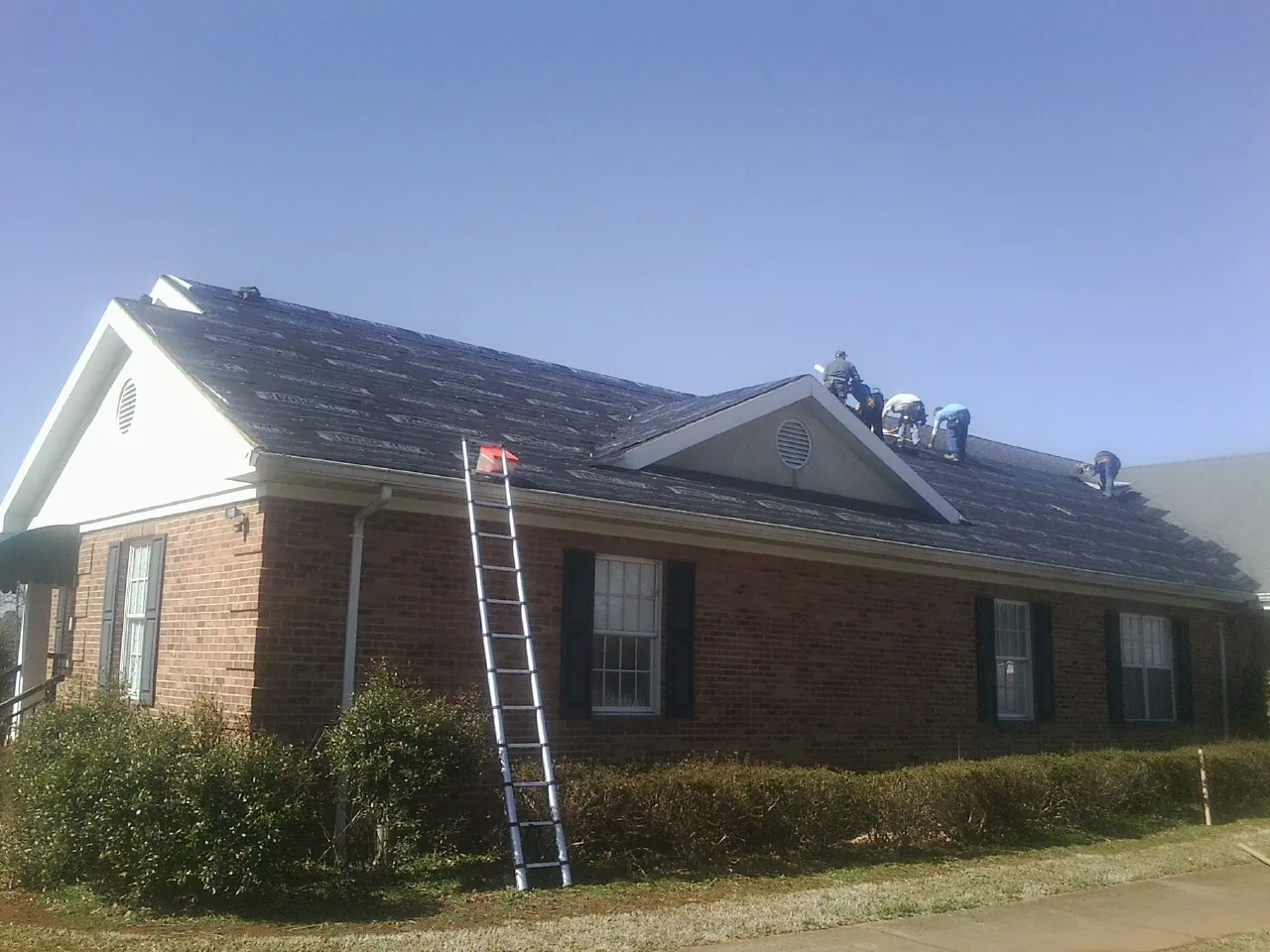 Crew tearing shingles off a brick ranch roof with a ladder set — Emergency Roof Repair work by our crew in Dennison